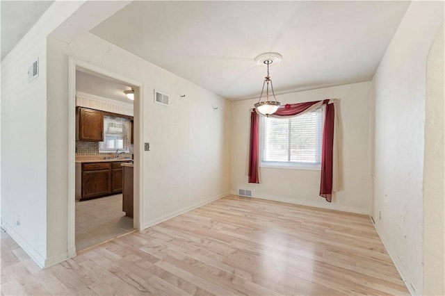 unfurnished dining area featuring light wood-style flooring, visible vents, and baseboards