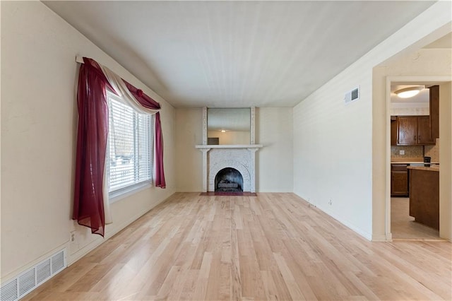 unfurnished living room featuring a brick fireplace, visible vents, and light wood finished floors