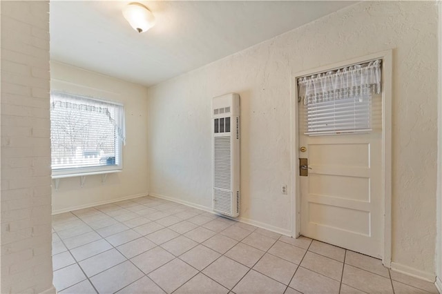 empty room featuring a textured wall, baseboards, and light tile patterned floors