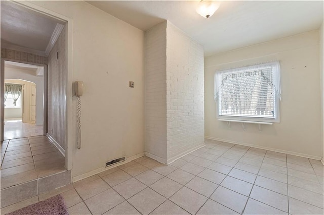 unfurnished room featuring arched walkways, light tile patterned floors, brick wall, visible vents, and baseboards