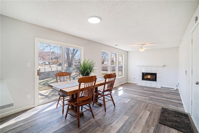 dining space featuring baseboards, a textured ceiling, a tiled fireplace, and wood finished floors