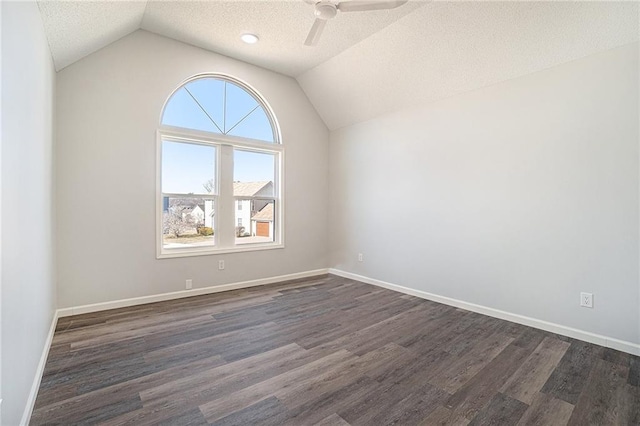 spare room featuring dark wood-type flooring, vaulted ceiling, a textured ceiling, and baseboards