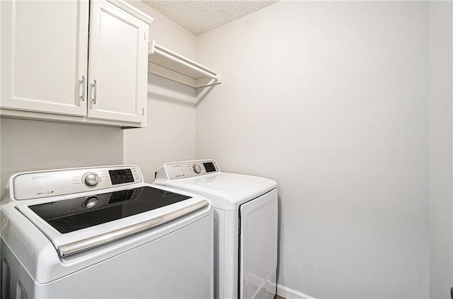 clothes washing area with cabinet space, a textured ceiling, and washing machine and clothes dryer