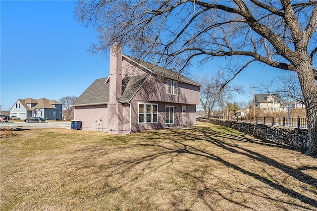 rear view of property with a lawn, a chimney, fence, and a residential view