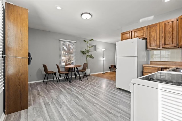 kitchen featuring white appliances, baseboards, light wood-type flooring, decorative backsplash, and brown cabinetry