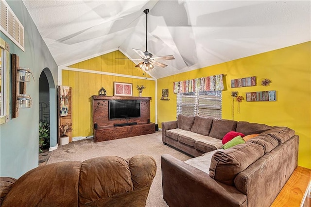 carpeted living room with arched walkways, wooden walls, a ceiling fan, visible vents, and vaulted ceiling