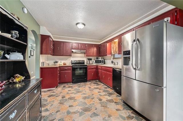 kitchen with arched walkways, stone finish flooring, a textured ceiling, under cabinet range hood, and black appliances