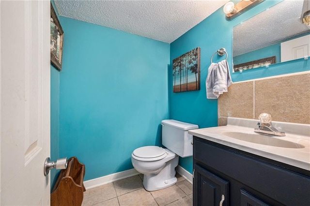 half bathroom featuring a textured ceiling, toilet, vanity, baseboards, and tile patterned floors