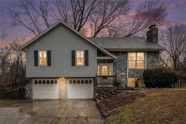 split level home with concrete driveway, stone siding, a chimney, and an attached garage