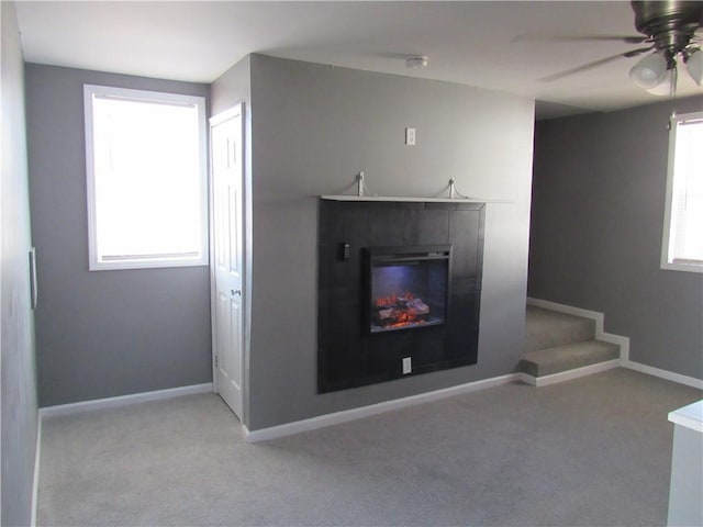 unfurnished living room featuring baseboards, ceiling fan, a glass covered fireplace, and light colored carpet