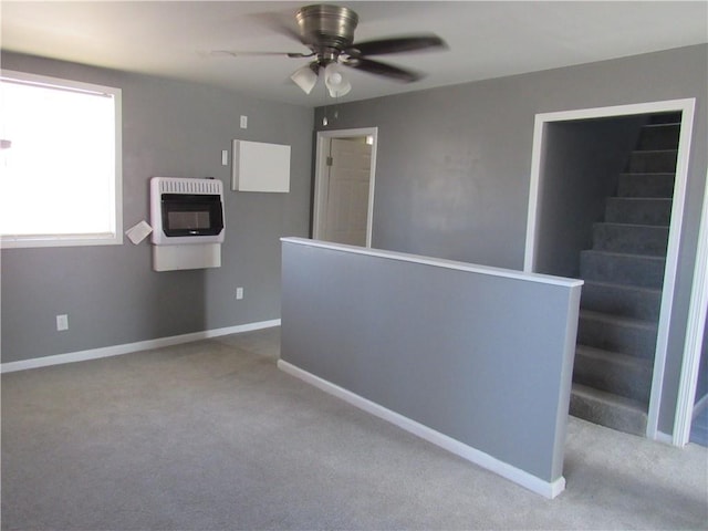 empty room with baseboards, light carpet, heating unit, and stairs