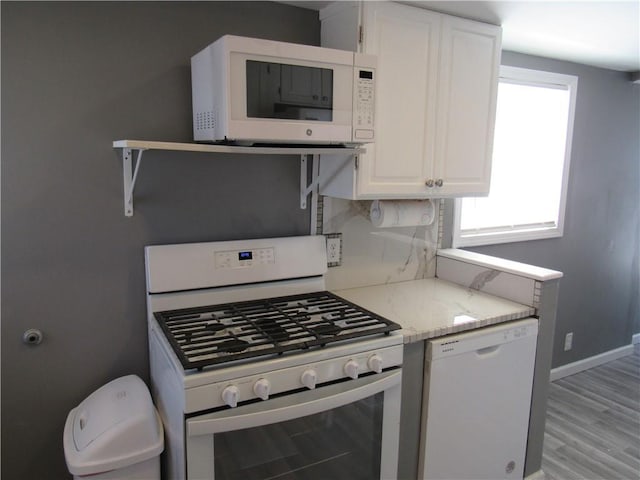 kitchen featuring white appliances, baseboards, white cabinets, light stone counters, and light wood-type flooring