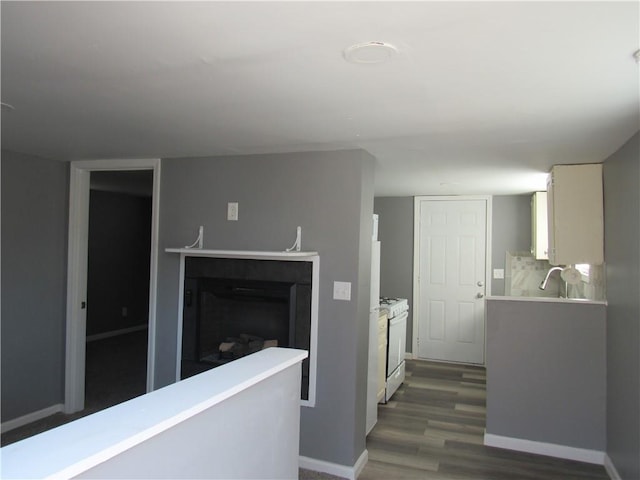 kitchen featuring white range with gas stovetop, baseboards, light countertops, a fireplace, and white cabinetry