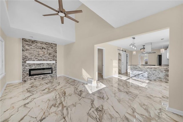 unfurnished living room with marble finish floor, a barn door, a fireplace, and a ceiling fan