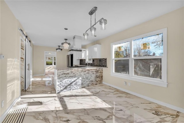 kitchen featuring a barn door, island range hood, white cabinets, hanging light fixtures, and freestanding refrigerator