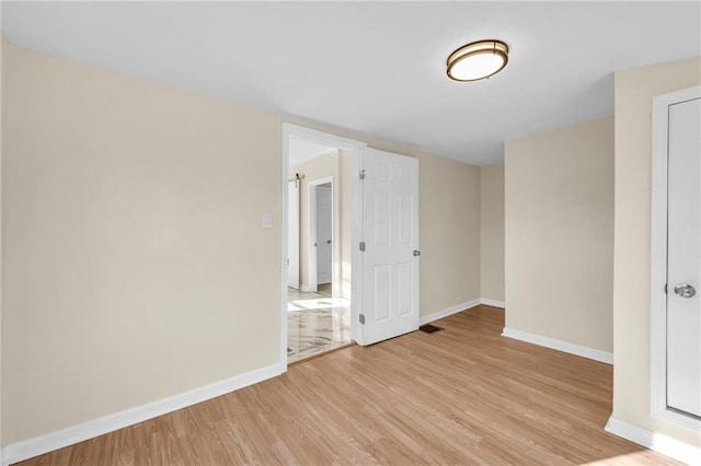 empty room featuring light wood finished floors, visible vents, and baseboards