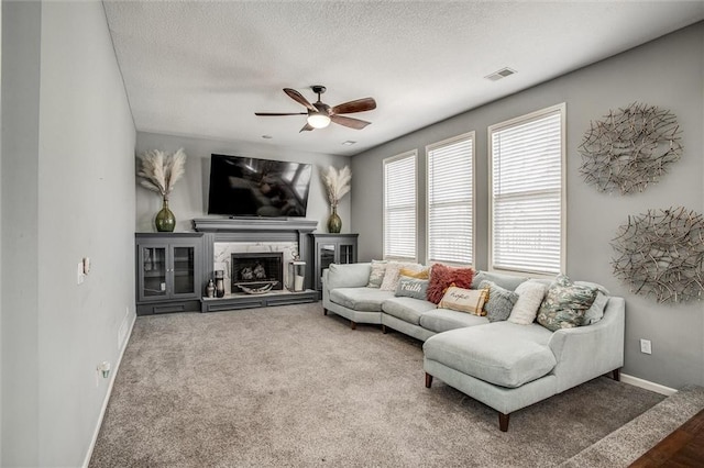 living room with a fireplace with raised hearth, baseboards, carpet flooring, a textured ceiling, and a ceiling fan