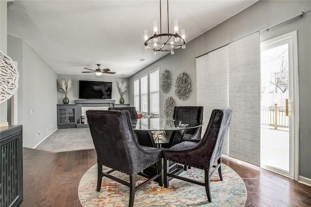 dining space featuring a textured ceiling, dark wood-type flooring, a fireplace, and ceiling fan with notable chandelier