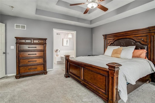 bedroom with visible vents, baseboards, a tray ceiling, light carpet, and ensuite bathroom