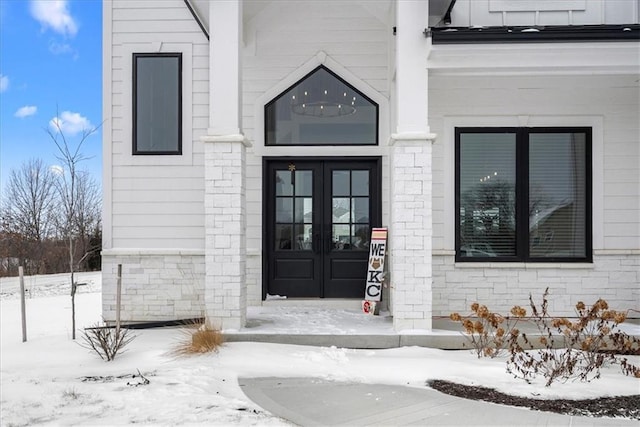 snow covered property entrance featuring stone siding and french doors