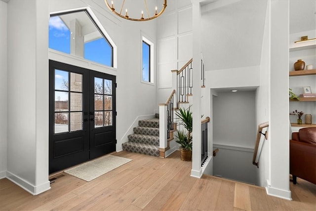 entryway with a towering ceiling, french doors, light wood finished floors, a chandelier, and stairs