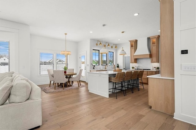 kitchen with premium range hood, light wood finished floors, light countertops, a kitchen breakfast bar, and open floor plan