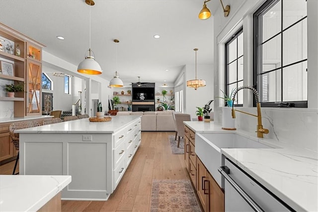 kitchen featuring open floor plan, dishwashing machine, light wood-style floors, brown cabinetry, and a sink