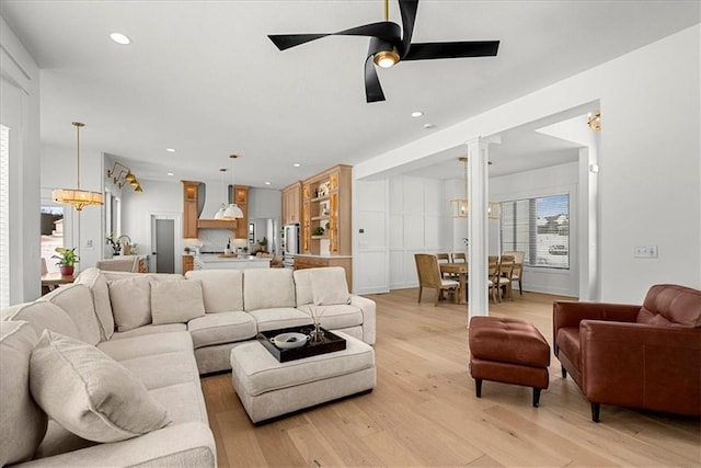 living room with recessed lighting, ceiling fan with notable chandelier, light wood-type flooring, and decorative columns