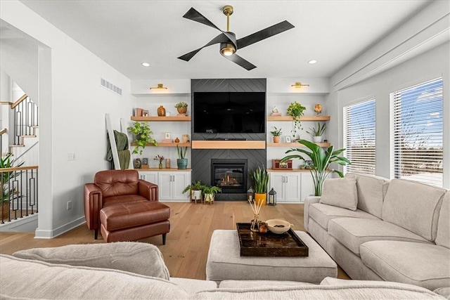 living room featuring visible vents, a ceiling fan, wood finished floors, a large fireplace, and stairs