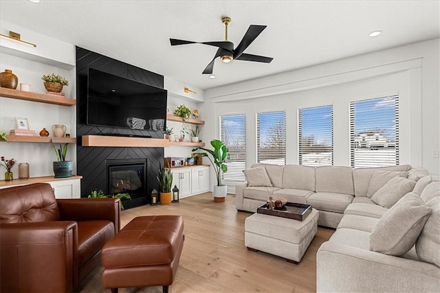 living room featuring light wood-type flooring, built in shelves, recessed lighting, a large fireplace, and ceiling fan