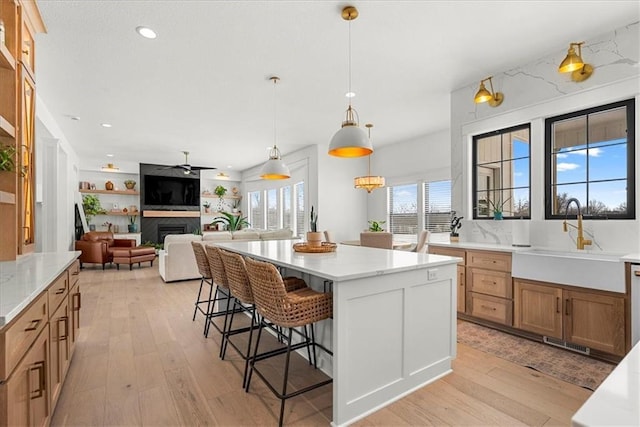 kitchen with a fireplace, a kitchen island, light wood-type flooring, and a sink