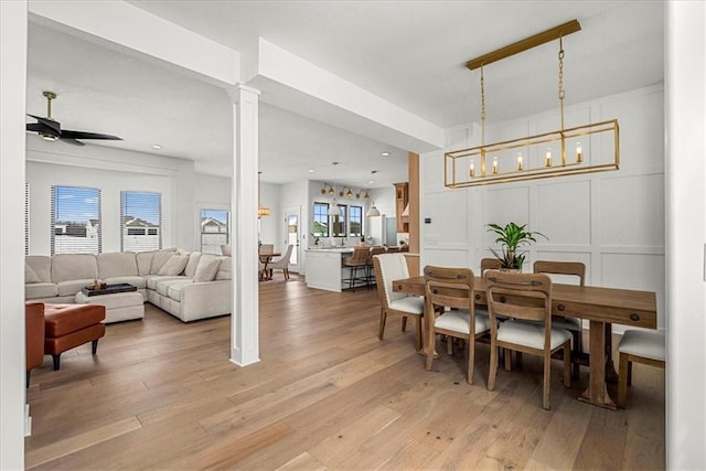 dining space featuring a ceiling fan, a decorative wall, decorative columns, and light wood-style flooring