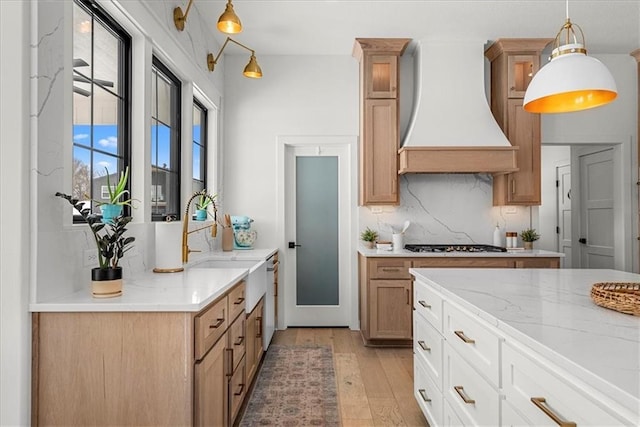 kitchen with light wood-type flooring, custom range hood, backsplash, hanging light fixtures, and stainless steel gas cooktop