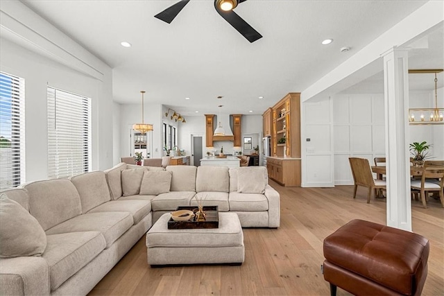 living area featuring ceiling fan with notable chandelier, decorative columns, light wood-style floors, and recessed lighting