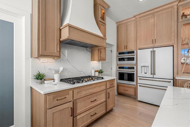 kitchen with light wood finished floors, multiple ovens, premium range hood, stainless steel gas stovetop, and high end fridge