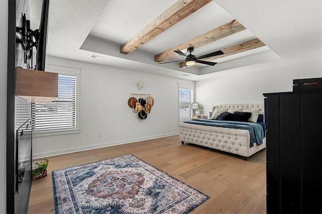 bedroom featuring a tray ceiling, multiple windows, baseboards, and wood finished floors