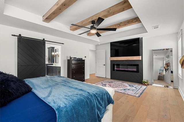 bedroom featuring visible vents, wood-type flooring, a glass covered fireplace, a barn door, and a raised ceiling