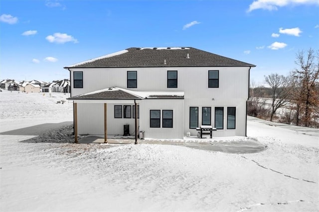 snow covered property with a shingled roof