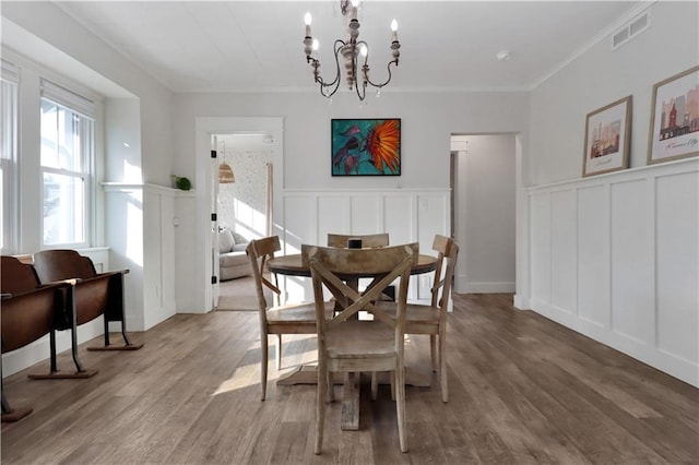 dining room featuring visible vents, ornamental molding, an inviting chandelier, wood finished floors, and a decorative wall