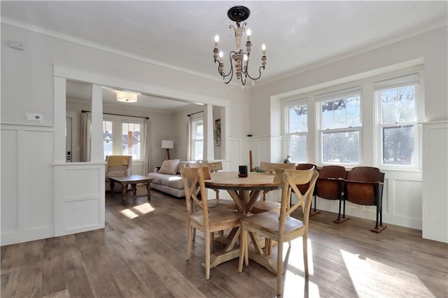 dining area with a wainscoted wall, wood finished floors, an inviting chandelier, crown molding, and a decorative wall