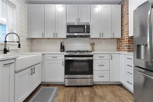 kitchen featuring a sink, appliances with stainless steel finishes, brick wall, light wood finished floors, and light countertops