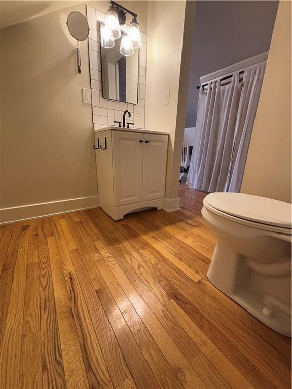 bathroom with toilet, wood finished floors, decorative backsplash, baseboards, and vanity