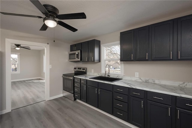 kitchen with baseboards, light stone counters, wood finished floors, stainless steel appliances, and a sink