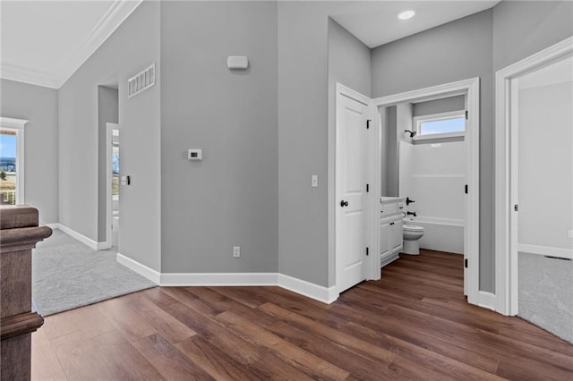 corridor with dark wood-style floors, visible vents, baseboards, and crown molding