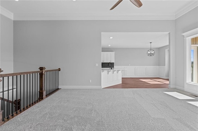 spare room with carpet floors, ornamental molding, and ceiling fan with notable chandelier