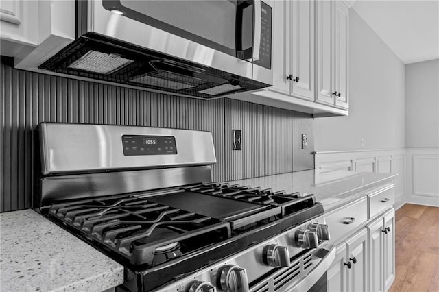 kitchen featuring light stone counters, white cabinetry, appliances with stainless steel finishes, wainscoting, and light wood-type flooring