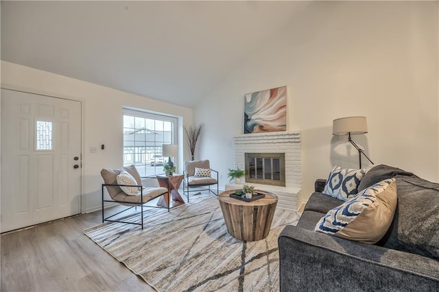 living room with high vaulted ceiling, a brick fireplace, and light wood-style flooring