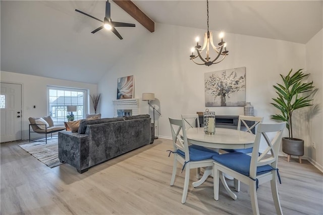 dining room featuring a fireplace, light wood-style flooring, beamed ceiling, and ceiling fan with notable chandelier