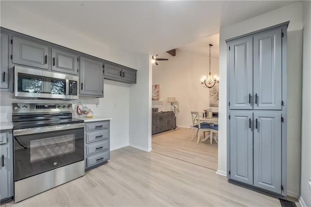 kitchen featuring stainless steel appliances, light countertops, light wood finished floors, decorative light fixtures, and an inviting chandelier