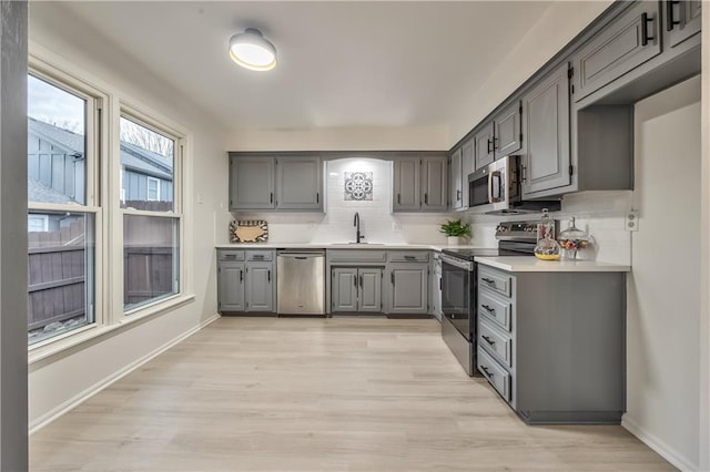 kitchen featuring a sink, stainless steel appliances, light countertops, and gray cabinetry